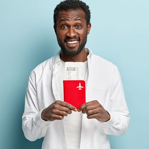 Imagem mostra homem sorrindo segurando um passaporte e uma passagem aerea