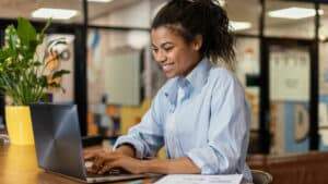 Imagem mostra moça sorrindo na frente do computador