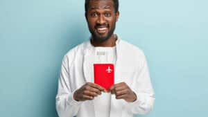 Imagem mostra homem sorrindo segurando um passaporte e uma passagem aerea