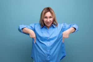 european blond young woman in casual shirt shows hands down at baner on blue background with copy space - fk partners